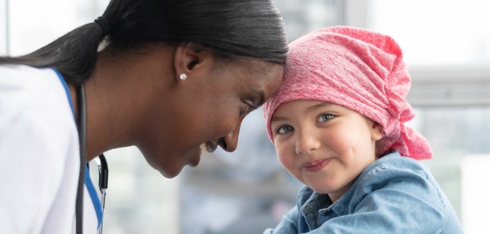 A cute elementary age girl with cancer is wearing a pink scarf on her head.
