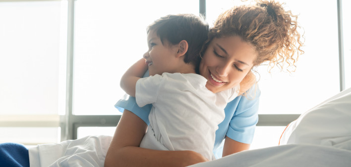 Beautiful sweet little boy hospitalized in the pediatrics ward hugging young nurse both smiling