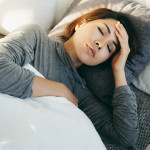 Young Asian woman with hand on forehead lying in bed and feeling sick