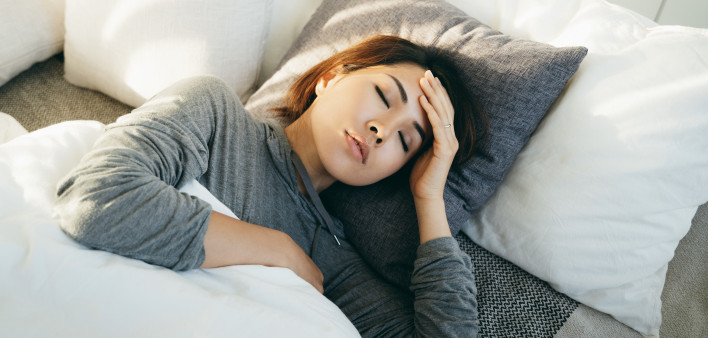 Young Asian woman with hand on forehead lying in bed and feeling sick