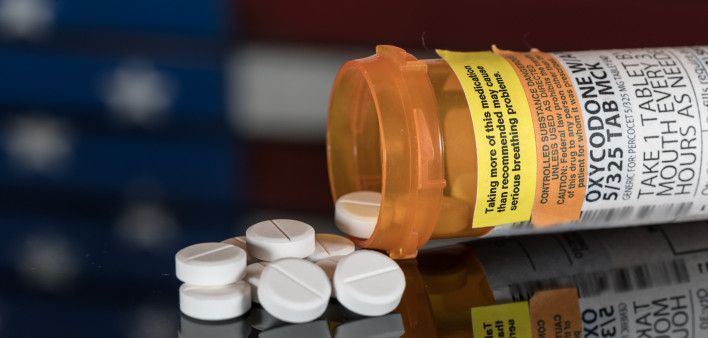 Prescription bottle for Oxycodone tablets and pills on wooden table with USA flag in background