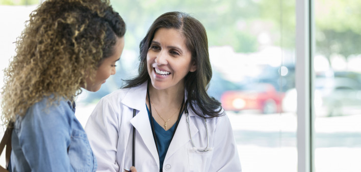 Caring mature female doctor shows test results to a young adult female patient. The doctor is smiling while talking with the patient