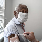 Nurse applying vaccine on patient's arm using face mask