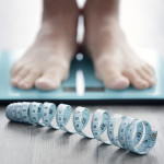 mans feet on scale with measuring tape on floor