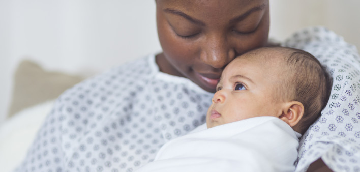 Beautiful African American mother in a hospital gown holds her newborn baby