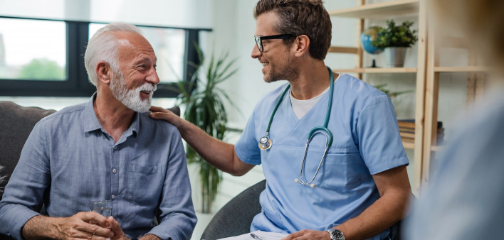 Happy doctor talking to senior male patient while being in a home visit.