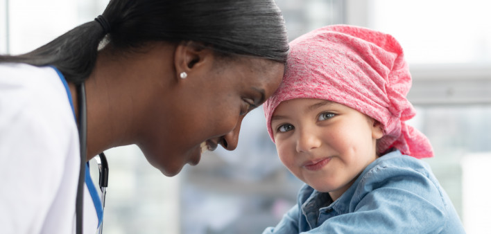 A cute elementary age girl with cancer is wearing a pink scarf on her head.