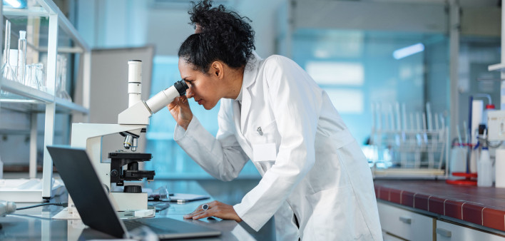 woman scientist in white lab coat looking into a microscope