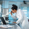woman scientist in white lab coat looking into a microscope