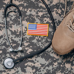 Top view of camouflaged military clothing, stethoscope, US flag and boots on wooden backgroun