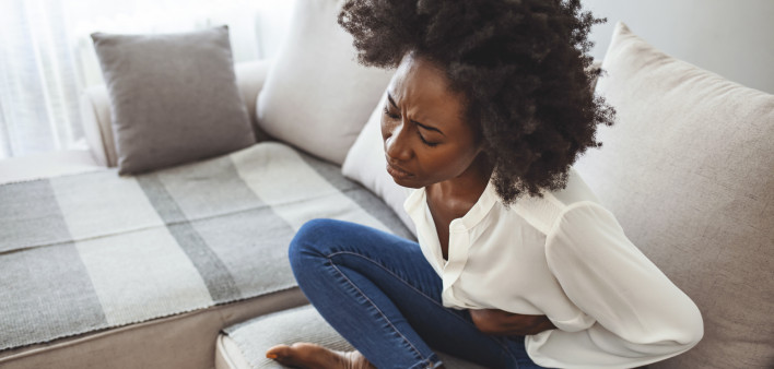 woman lying on her sofa alone and suffering from period cramps