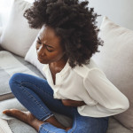 woman lying on her sofa alone and suffering from period cramps