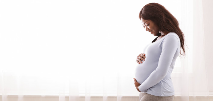 Beautiful pregnant afro woman hugging her tummy,