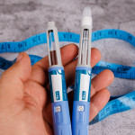 Hand with semaglutide pens and measuring tape on cement surface stock photo Adults Only, Beauty Treatment, Biotechnology, Blood, Blood Sugar Test