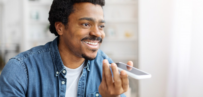 Smiling Young Black Man Recording Voice Message On Smartphone At Home, Millennial African American Guy Using Modern Mobile Phone