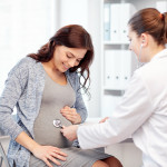 pregnancy, gynecology, medicine, health care and people concept - gynecologist doctor with stethoscope listening to pregnant woman baby heartbeat