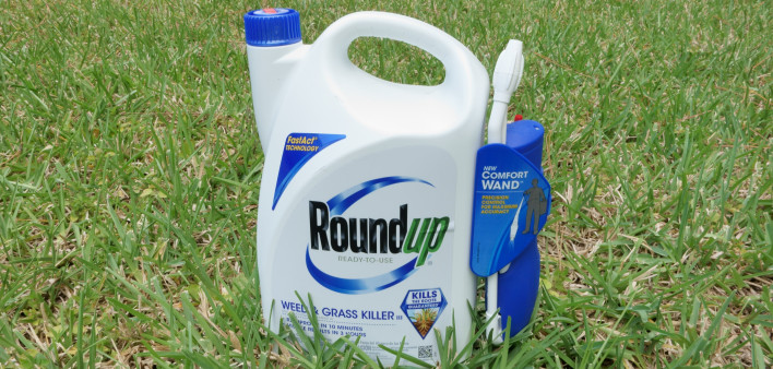 A container of Roundup Weed and Grass Killer on a grass lawn.
