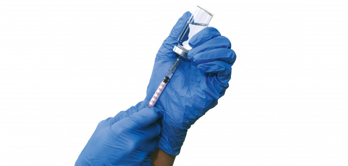 hands with blue gloved filling a syringe from a vial of vaccine