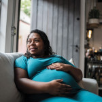 Pregnant Black woman holder her belly on couch