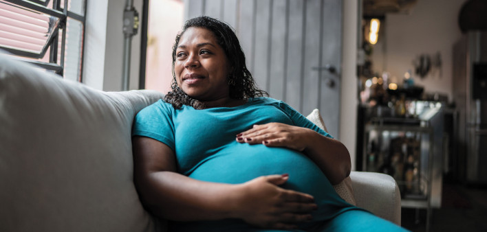 Pregnant Black woman holder her belly on couch