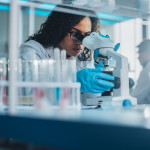 Medical Science Laboratory: Portrait of Beautiful Black Scientist Looking Under Microscope