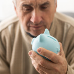 Senior caucasian man holding piggy bank with glasses depressed and worry for distress, crying angry and afraid.