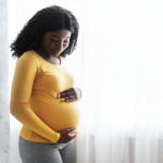 Beautiful pregnant african woman hugging her tummy