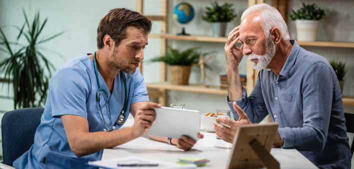 Worried senior patient and his doctor using touchpad during medical appointment