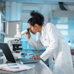 woman scientist in white lab coat looking into a microscope