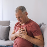 Severe heartache, man suffering from chest pain, having heart attack or painful cramps, pressing on chest with painful expression. Photo of Mature man suffering from chest pain at home during the day.