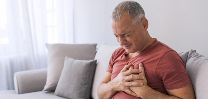 Severe heartache, man suffering from chest pain, having heart attack or painful cramps, pressing on chest with painful expression. Photo of Mature man suffering from chest pain at home during the day.