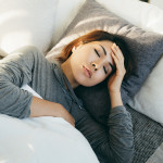 Young Asian woman with hand on forehead lying in bed and feeling sick
