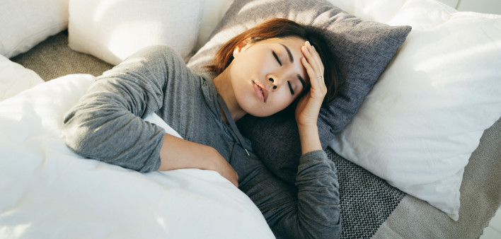 Young Asian woman with hand on forehead lying in bed and feeling sick