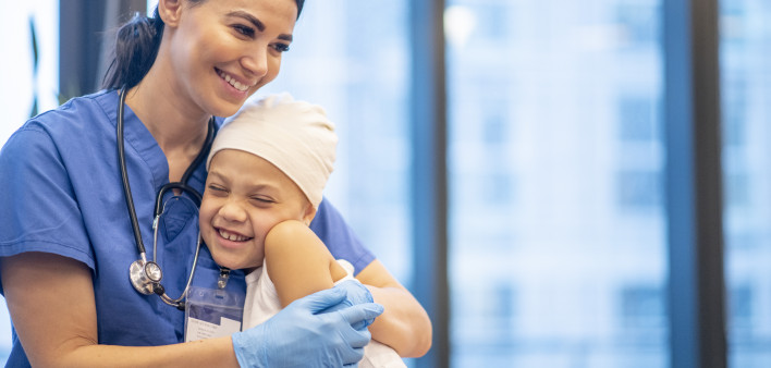 Nurse Hugging Young Cancer Patient stock photo A young Latin female nurse hugs her cancer patient as they enjoy a brief moment together. The young girl is smiling and happy. The nurse is wearing blue scrubs with a stethoscope around her neck, while the yo