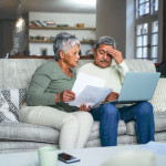 Shot of a senior couple looking stressed while using a laptop and going through paperwork on the sofa