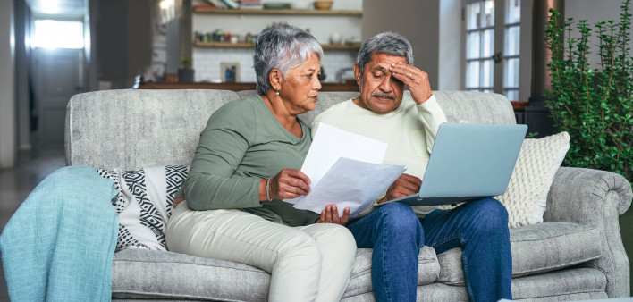 Shot of a senior couple looking stressed while using a laptop and going through paperwork on the sofa