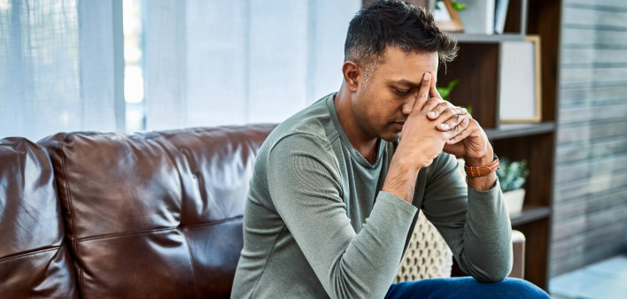 Shot of a man looking stressed while sitting on the sofa at home