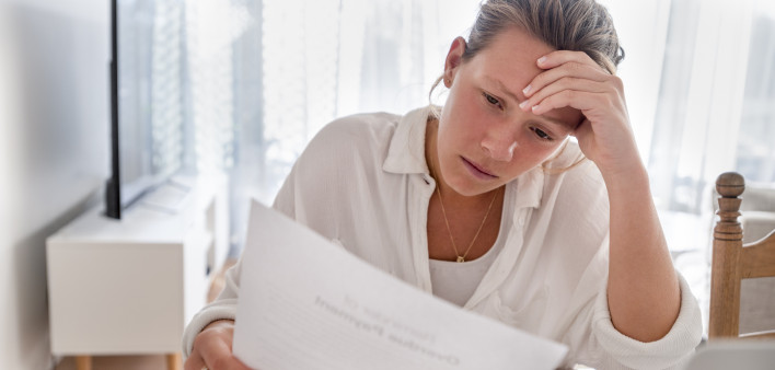 Woman looking worried holding paperwork at home. She is reading a financial bill or a letter with bad news. She looks very stressed and upset.