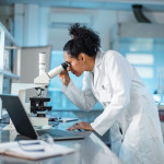 woman scientist in white lab coat looking into a microscope