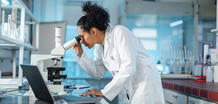 woman scientist in white lab coat looking into a microscope