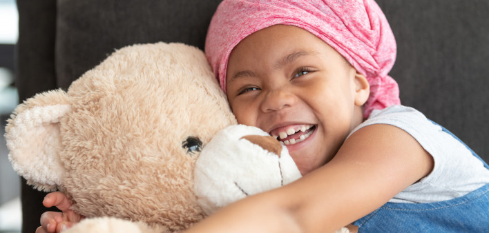 Happy girl with cancer hugs large teddy bear