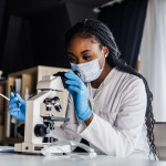 female scienitst analyzing a sample under a microscope while doing research