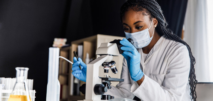 female scienitst analyzing a sample under a microscope while doing research