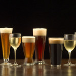 An assortment of glasses of wine and beer including a classic pilsner flute, a sparkling wine glass, an American half pint glass, a weizen or wheat beer glass, an American pint glass, a white wine glass, and a red wine glass.