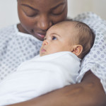 Beautiful African American mother in a hospital gown holds her newborn baby