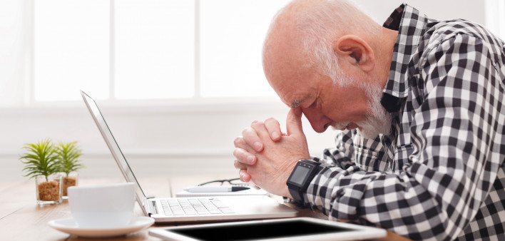 Worried senior man using laptop at home.