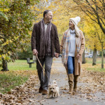 Full length view of Caucasian man and woman in 50s and 60s holding hands and talking as they enjoy exercising amidst colorful fall foliage.