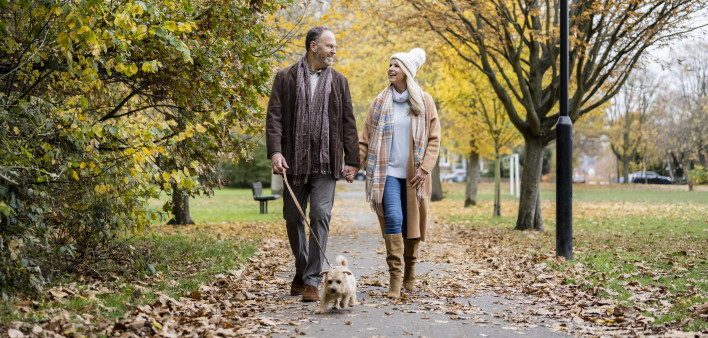 Full length view of Caucasian man and woman in 50s and 60s holding hands and talking as they enjoy exercising amidst colorful fall foliage.