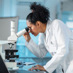 woman scientist in white lab coat looking into a microscope