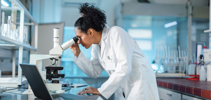 woman scientist in white lab coat looking into a microscope